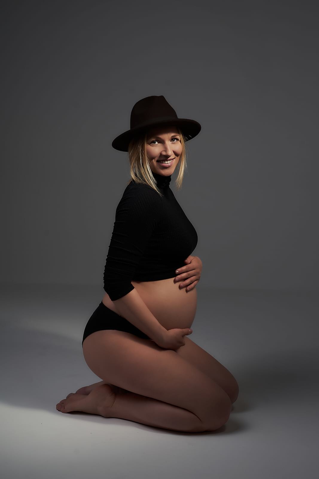 Holkerben térdel a kismama és mosolyog